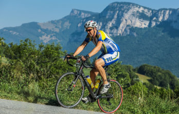 A man dressed in biking outfit riding uphill on a bike with green field in the foreground and the mountains in the background near Happy Acres RV Park in Pueblo Colorado